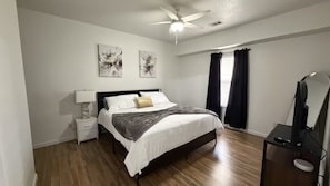 A bedroom with a bed, a nightstand, a desk, a ceiling fan, and artwork on the wall. - A8 • Cozy Stay • Pool • Close to A-State & Dining (Jonesboro)
