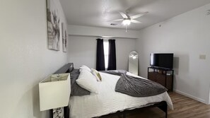 Una camera da letto con un letto, una ventola a soffitto, una televisione e uno specchio.
