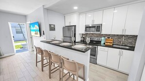 Une cuisine moderne avec des meubles blancs, des appareils en acier inoxydable et un coin bar avec des tabourets.