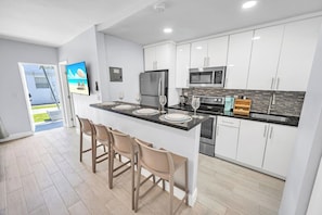 Une cuisine moderne avec des meubles blancs, des appareils en acier inoxydable et un coin bar avec des tabourets.