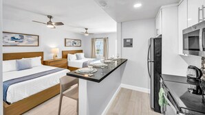 Une chambre d’hôtel équipée d’un lit, de tables de chevet, d’un bureau avec une chaise, d’un réfrigérateur, d’un four à micro-ondes et d’un ventilateur de plafond.
