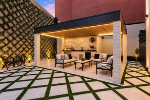 An outdoor patio area with a covered seating arrangement, a grill, and a decorative wall with greenery. - Luxury Poolside Suite | 4 King Beds+Sleeper Sofa (New Orleans)