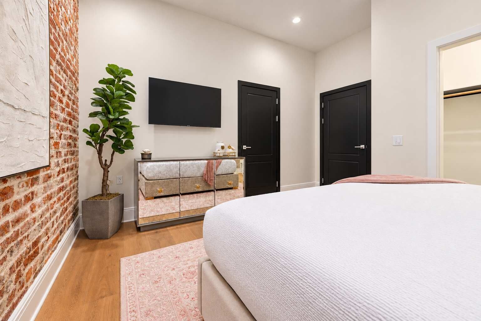 Un dormitorio con cama, cómoda, planta en maceta y televisor de pantalla plana en la pared.