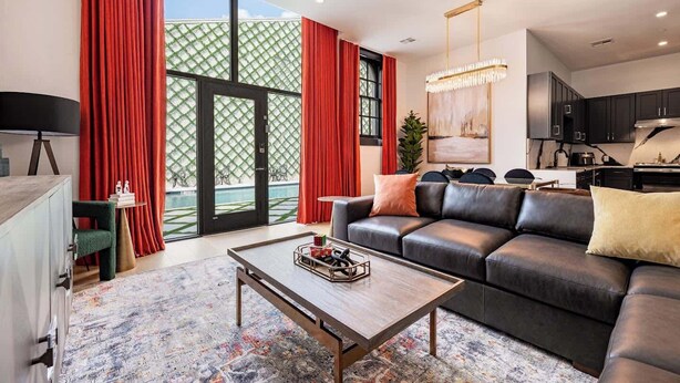 A modern living room with a leather sofa, a coffee table, and a view of a pool through large windows. - Luxury Poolside Suite | 4 King Beds+Sleeper Sofa (New Orleans)
