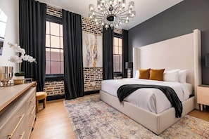 A bedroom with a large bed, a dresser, a chandelier, and a brick wall.