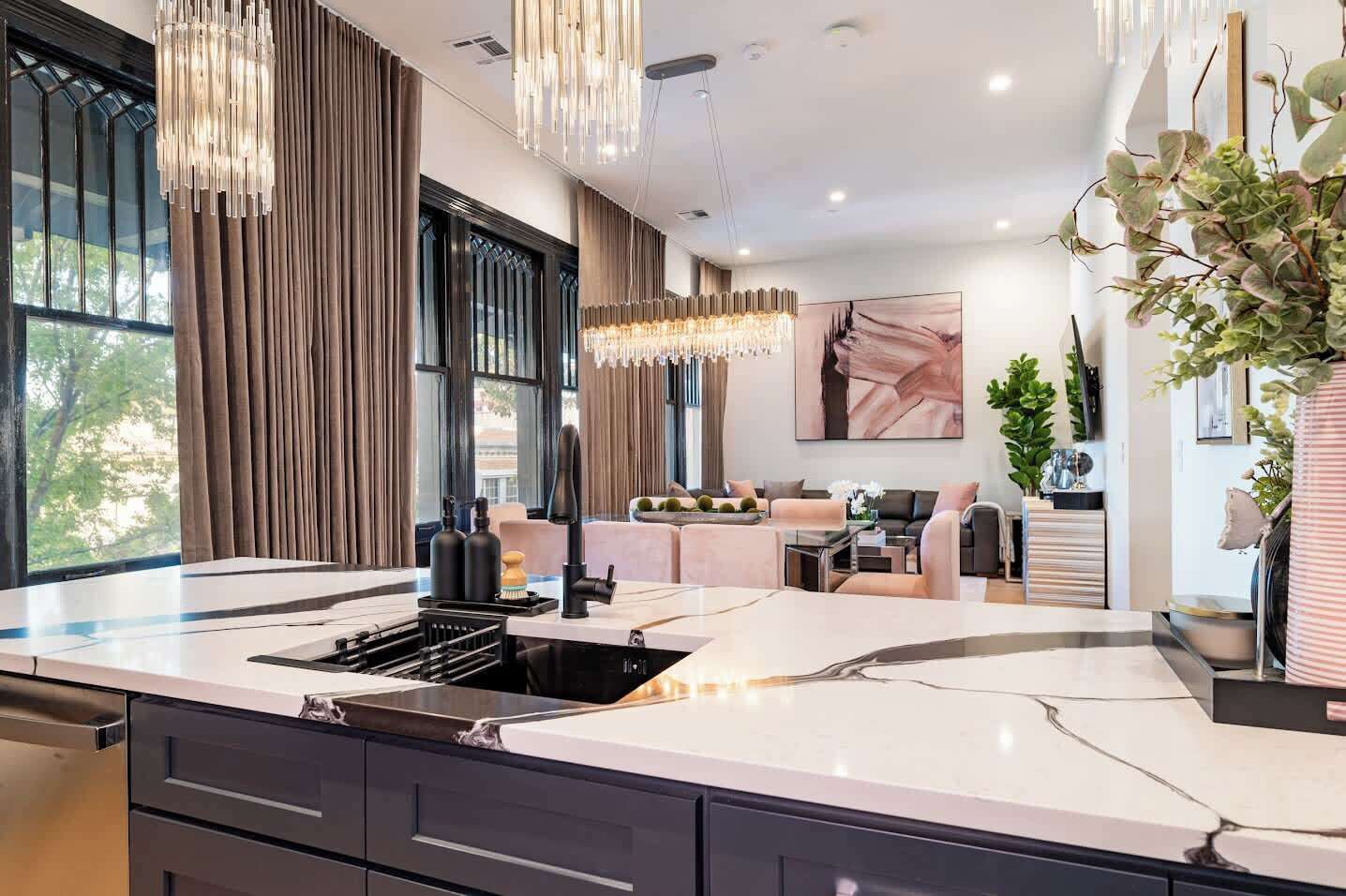 A modern kitchen with a large island, pendant lighting, and a view of the living area.