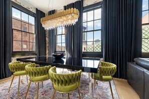 A dining area with a black table, green upholstered chairs, a chandelier, and large windows with curtains.