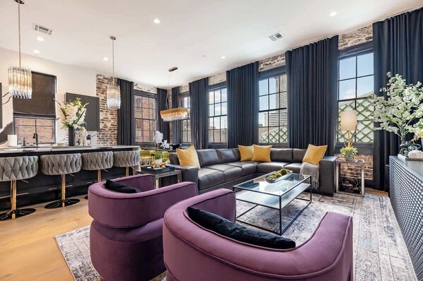 A modern living room with a sectional sofa, a glass coffee table, and purple armchairs.