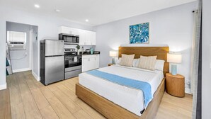 A modern hotel room with a wooden bed, a kitchenette, and a bathroom. - Hawksbill 105 | Beach & Pool Studio | Walkable (Lauderdale-by-the-Sea)