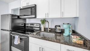 A modern kitchen with white cabinets, a stainless steel refrigerator, a microwave, a stove, a sink, and a coffee maker. - Hawksbill 105 | Beach & Pool Studio | Walkable (Lauderdale-by-the-Sea)
