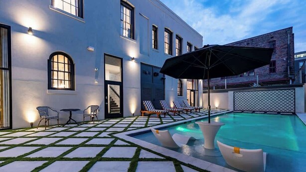 A pool area with lounge chairs, a table, and a covered seating area. - On Streetcar Line | 5 King Beds | Blackout Drapes (New Orleans)