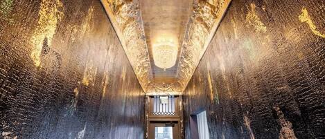 A corridor with ornate wall patterns and a chandelier.
