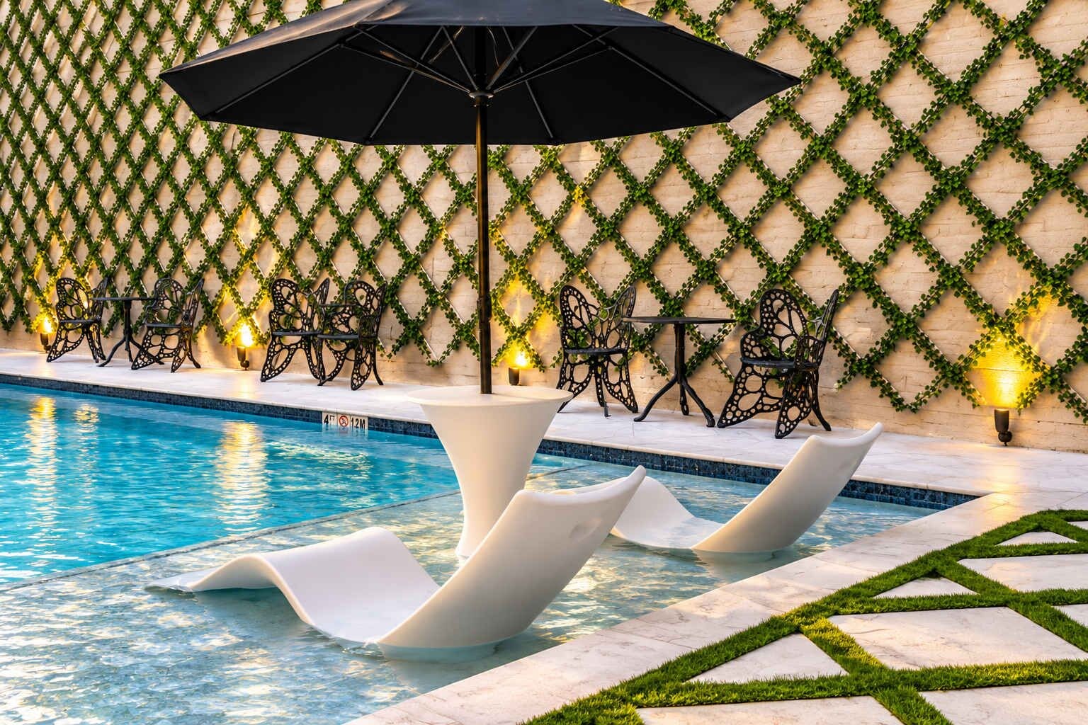 Un área de piscina con sillones reclinables y mesas, rodeada por un muro decorado.