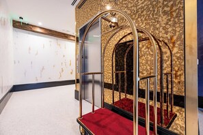 A hallway with a marble wall, a red carpeted area, and a metal structure with glass panels. - On Streetcar Line | 5 King Beds | Blackout Drapes (New Orleans)