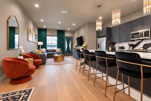 A modern living room with a sofa, chairs, a coffee table, and a kitchen area with a bar and seating. - On Streetcar Line | 5 King Beds | Blackout Drapes (New Orleans)
