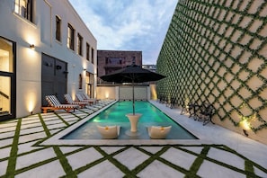 Une piscine avec des chaises longues, une table et un mur décoratif agrémenté de plantes.