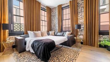 A modern bedroom with a large bed, dark curtains, and a brick wall.