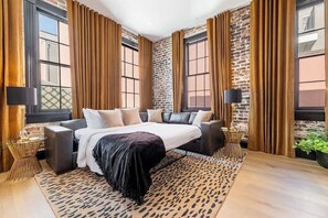 A modern bedroom with a large bed, dark curtains, and a brick wall.
