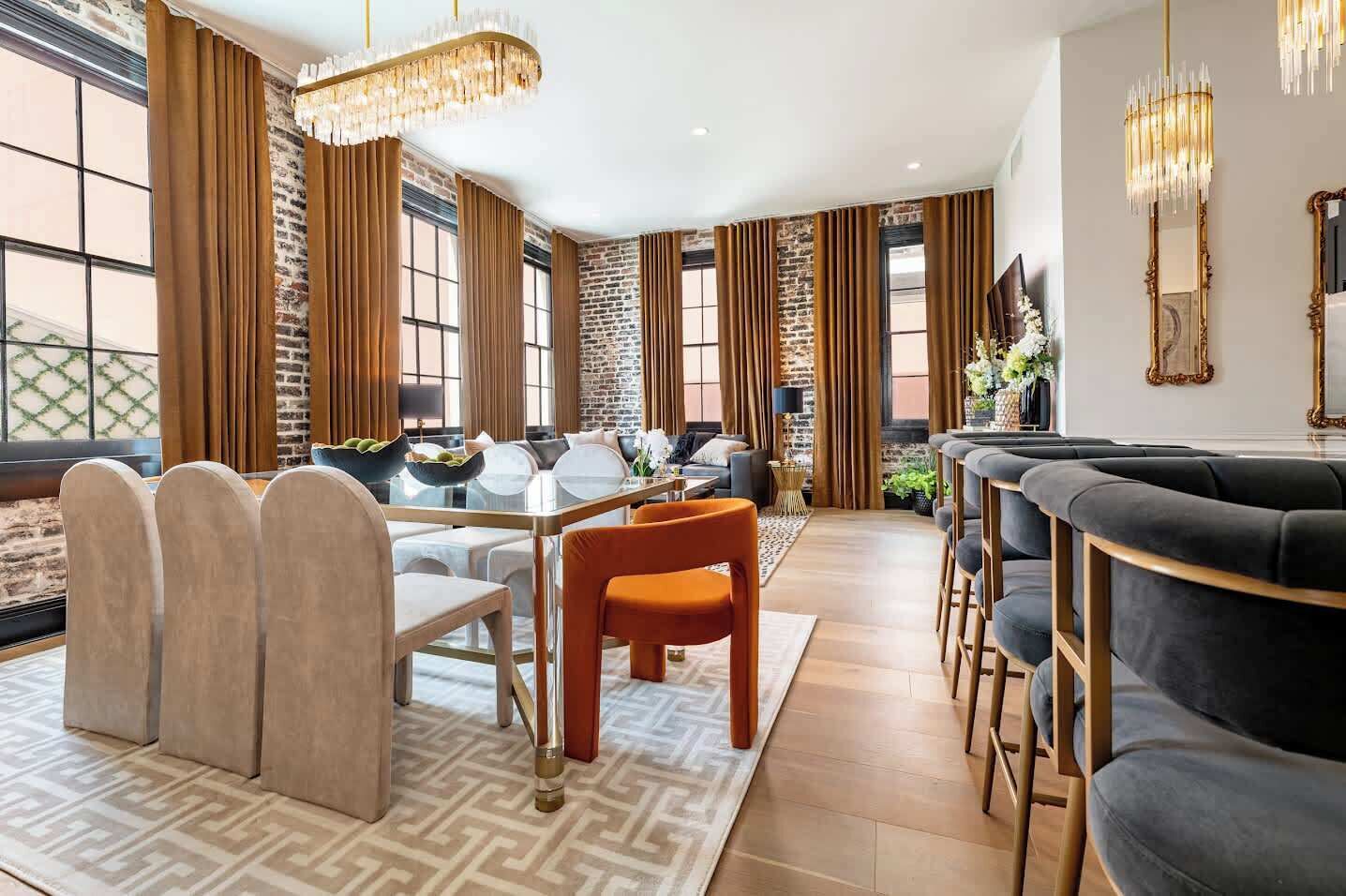 A modern living room with a dining area, large windows, and a brick wall.