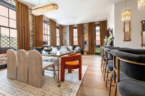 A modern living room with a dining area, large windows, and a brick wall.