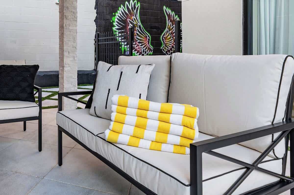 A modern outdoor seating area with a sofa and chairs, a decorative wall with a winged design, and a concrete floor.