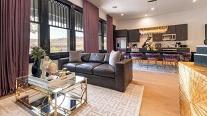 Un salón moderno con un sofá de cuero oscuro, una mesa de centro de vidrio y vistas a la ciudad a través de amplios ventanales.