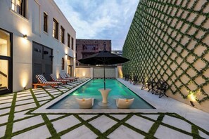 Une piscine avec des chaises longues, une table et un mur décoratif agrémenté de plantes.