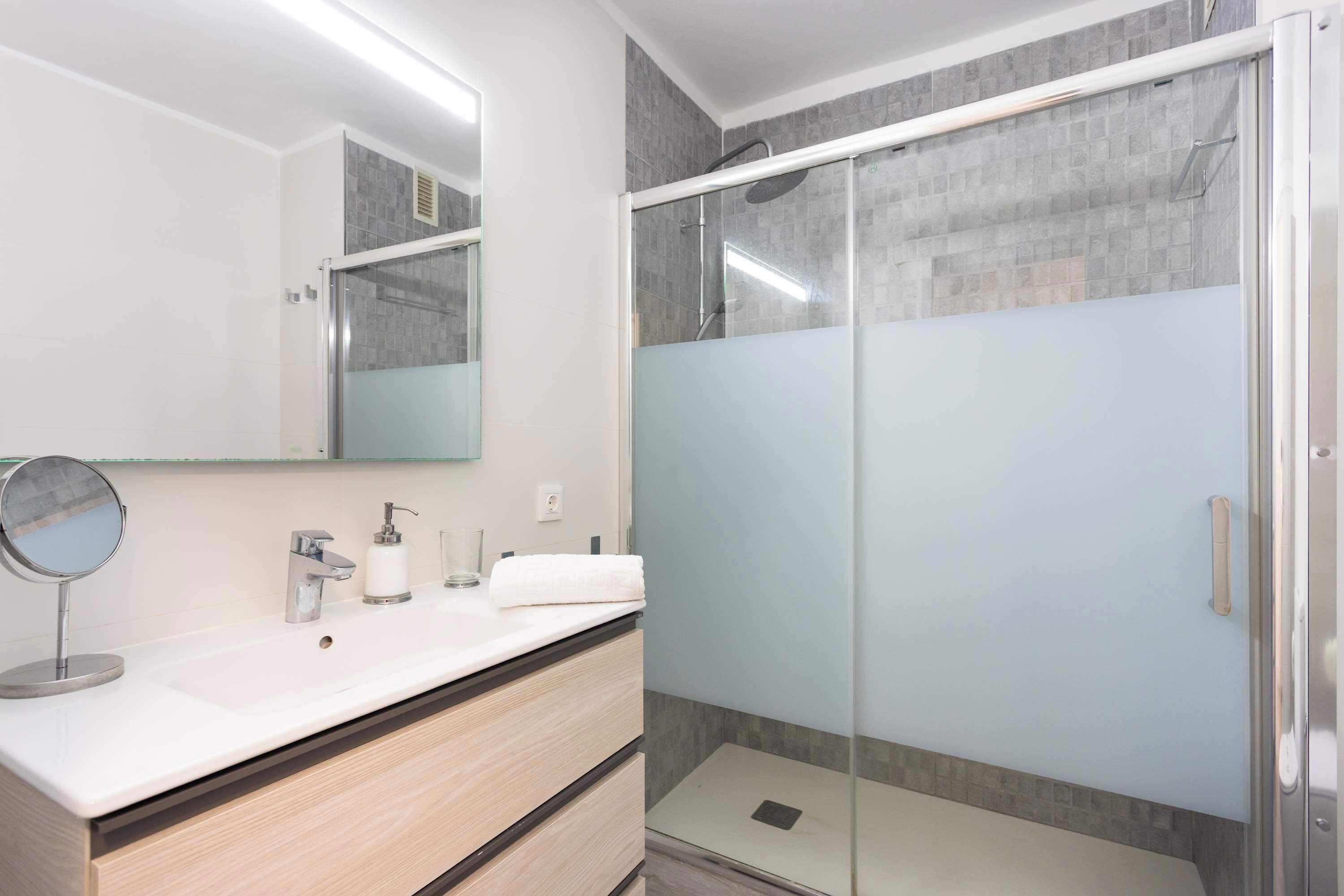 A modern bathroom with a glass-enclosed shower, a white sink with a mirror, and a towel rack.