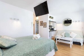 Ein modernes Hotelzimmer mit Bett, Sofa, einem flachbildfernseher an der Wand, einem runden Spiegel und einer Küchenzeile.
