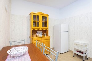 Ein Essbereich mit einem Holztisch, Stühlen, einem weißen Korb, einem gelben Schrank und einem weißen Kühlschrank.