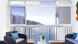 A balcony with wicker furniture, a bottle, and glasses, overlooking a coastal view. - Apartamento Vistas Al Mar y Al Teide (Tacoronte)