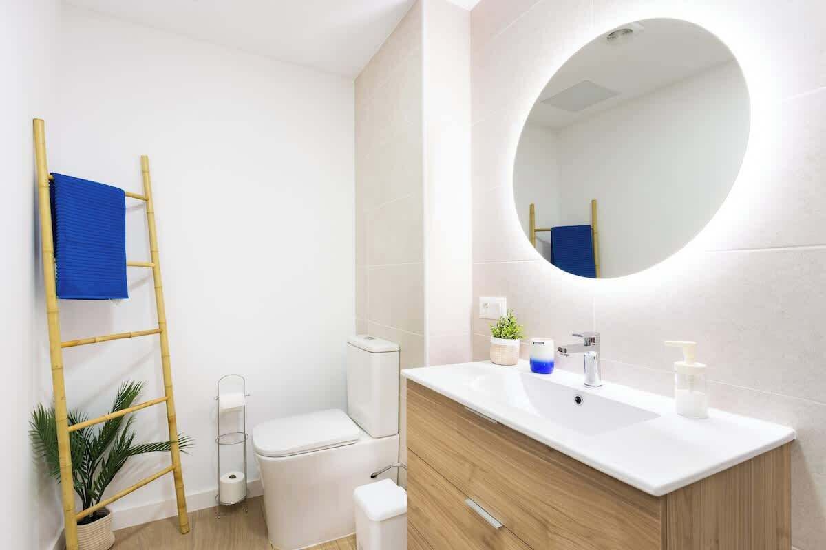 Ein modernes Badezimmer mit Toilette, Bidet, Waschbecken, Spiegel und einem blauen Handtuch auf einer Bambusleiter.