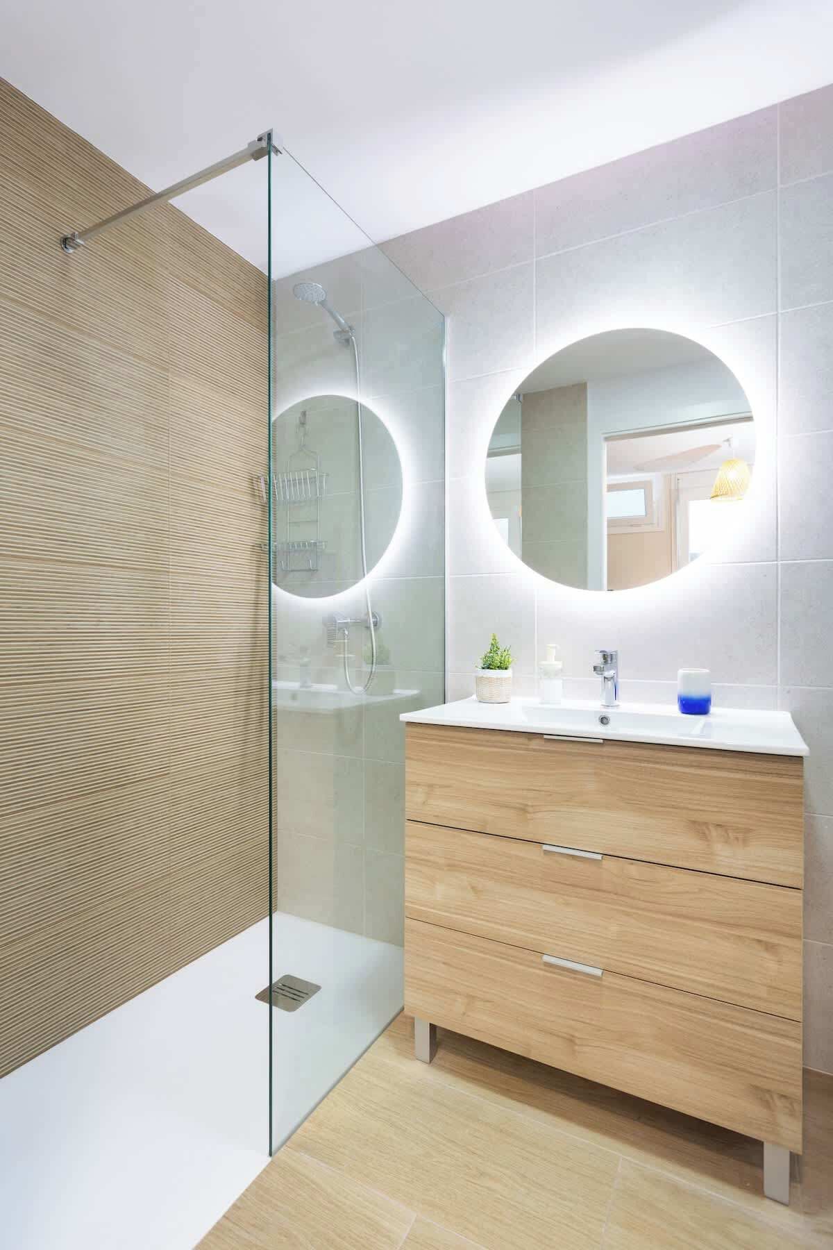 A modern bathroom with a glass-enclosed shower, a wooden vanity with a mirror, and a white sink.