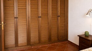 Een slaapkamer met een grote houten garderobe, een nachtkastje met een lamp en een bloemenbedekking.