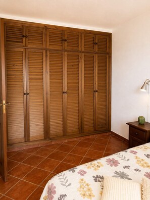 Ein Schlafzimmer mit großem Holzschrank, Nachttisch mit Lampe und floralem Bettbezug.