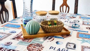 Een eettafel met een placemat waarop afbeeldingen van een strand en zee staan, een waterfles, een groene kom en een gevlochten mand met decoratieve spullen.
