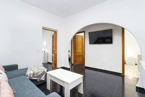 Ein modernes Wohnzimmer mit einer Couch, einem weißen Tisch und einem an einer Bogenwand befestigten Fernseher.
