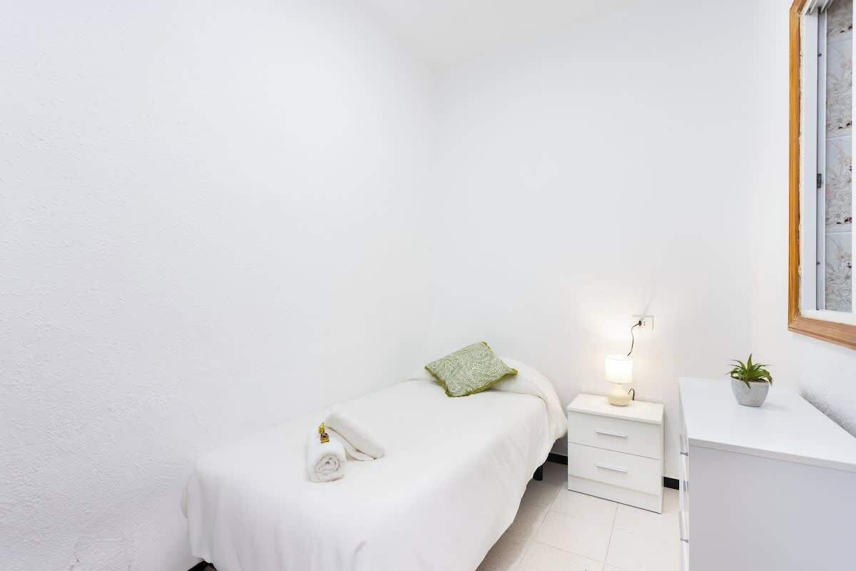 Ein kleines, sauberes Zimmer mit einem Einzelbett, einem Nachttisch mit Lampe und einem kleinen Topfpflanzen.