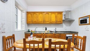 A kitchen with wooden cabinets, a granite countertop, and a dining table with chairs. - Apartamento Campo Rosa Tacoronte (Tacoronte)