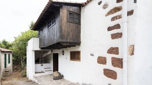 Um edifício com escadaria de pedra que leva a uma porta de madeira, um pequeno muro de pedra e fachada branca com áreas em castanho.