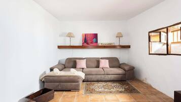 Een woonkamer met een bank, een voetenbankje en een vloerkleed.