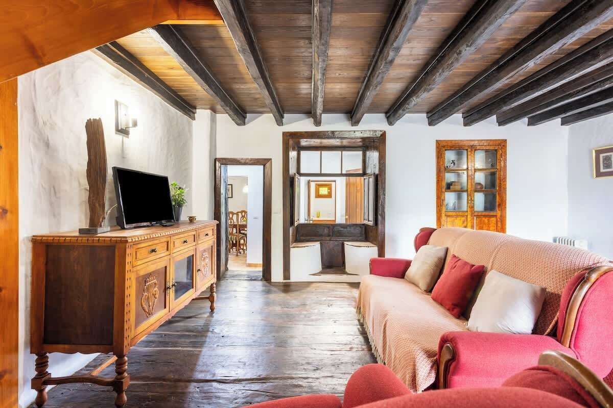 A room with a wooden ceiling, a wooden cabinet, a television, a sofa, and a cabinet with glass doors.