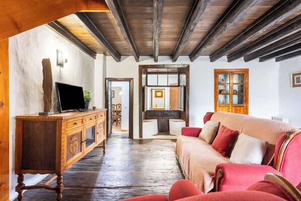 A room with a wooden ceiling, a wooden cabinet, a television, a sofa, and a cabinet with glass doors.