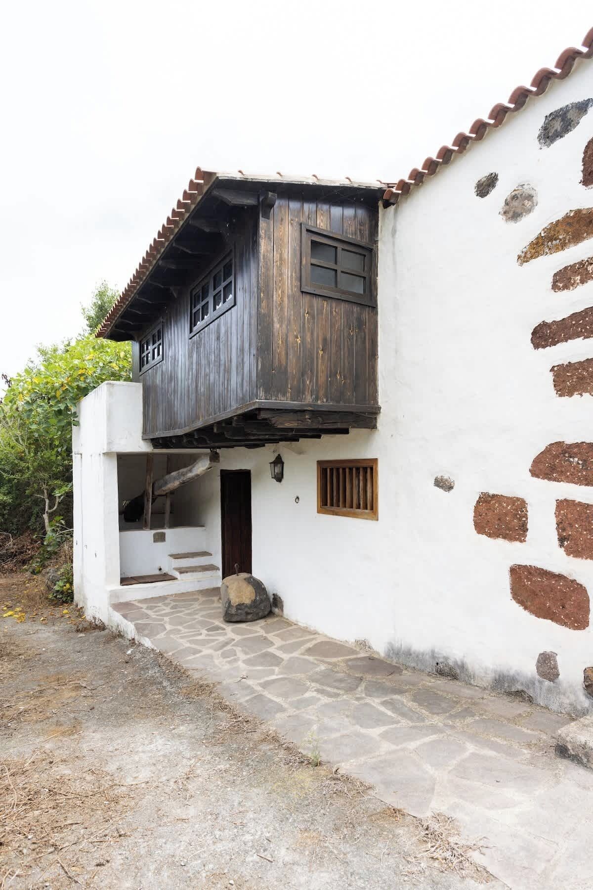 Un edificio rústico con una escalera de piedra que lleva a una puerta de madera, rodeado por un muro blanco con manchas marrones.