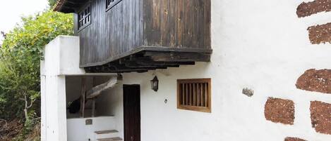 Un edificio rústico con una escalera de piedra que lleva a una puerta de madera, rodeado por un muro blanco con manchas marrones.
