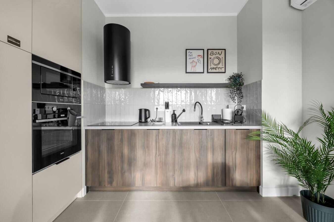 Una cocina moderna con horno empotrado, campana extractora negra, un lavabo y encimera de madera. Hay dos cuadros enmarcados en la pared sobre el lavabo.