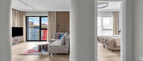 A modern living room with a sofa, a coffee table, a TV, and a balcony with curtains.