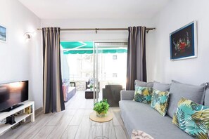 A modern living room with a flat-screen TV, grey sofa, and a small round table with a plant. - Apartamento Terraza Martianez (Puerto de la Cruz)