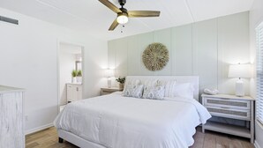 Una camera da letto con un letto, un ventilatore a soffitto, un elemento decorativo a parete, lampade da comodino e un comodino.