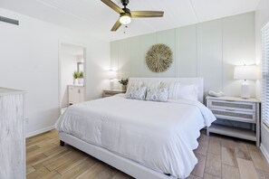 Ein Schlafzimmer mit Bett, Deckenventilator, Wanddeko, Nachttischlampen und einem Nachttisch.